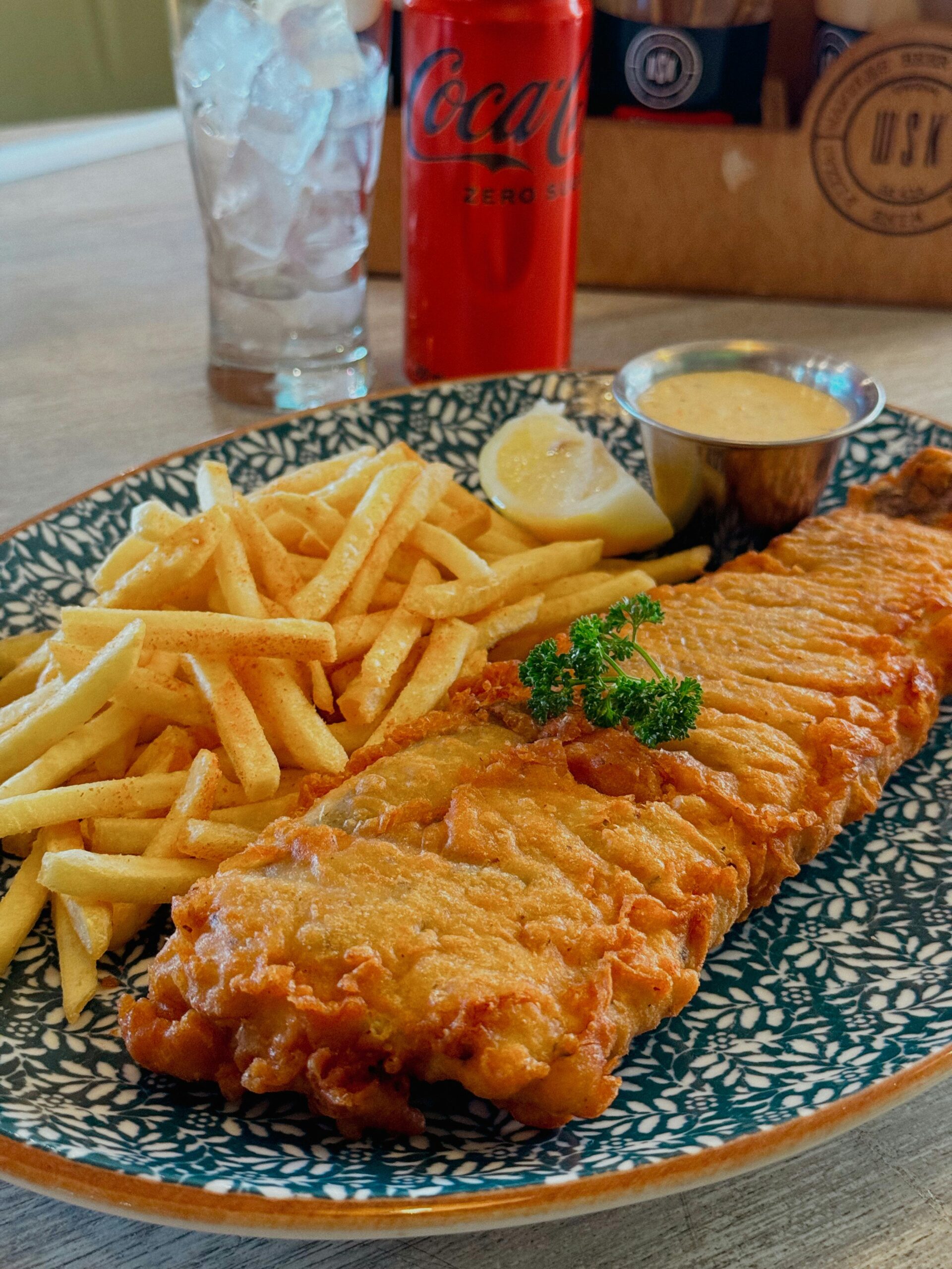 A delectable plate of golden fish and chips served with a refreshing soda.